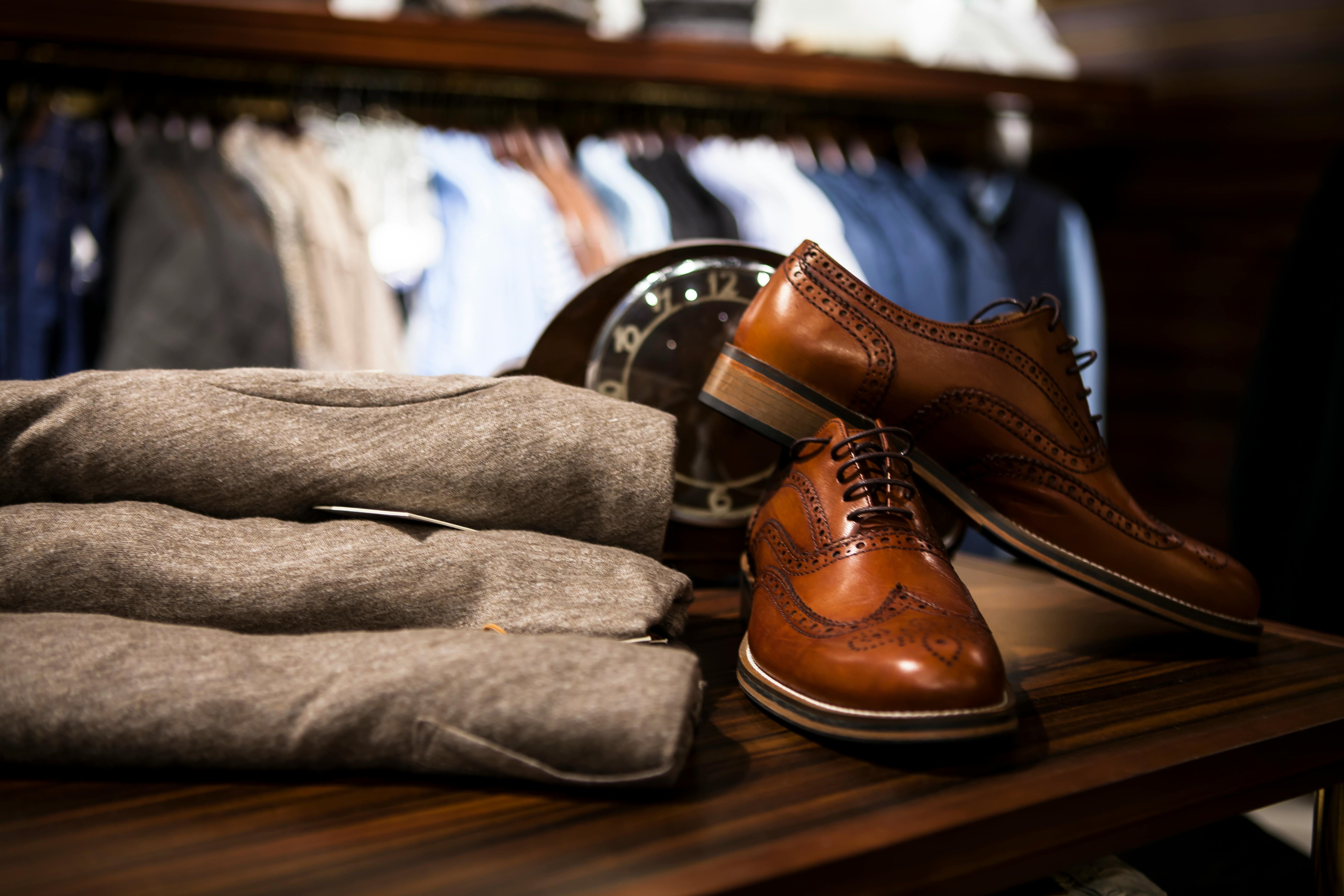 pair-of-brown-leather-wingtip-shoes-beside-gray-apparel-on-wooden-surface