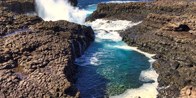 Buracona - The Blue Eye of Cabo Verde - blue lagoon inside a black rock with ocean splash in the back